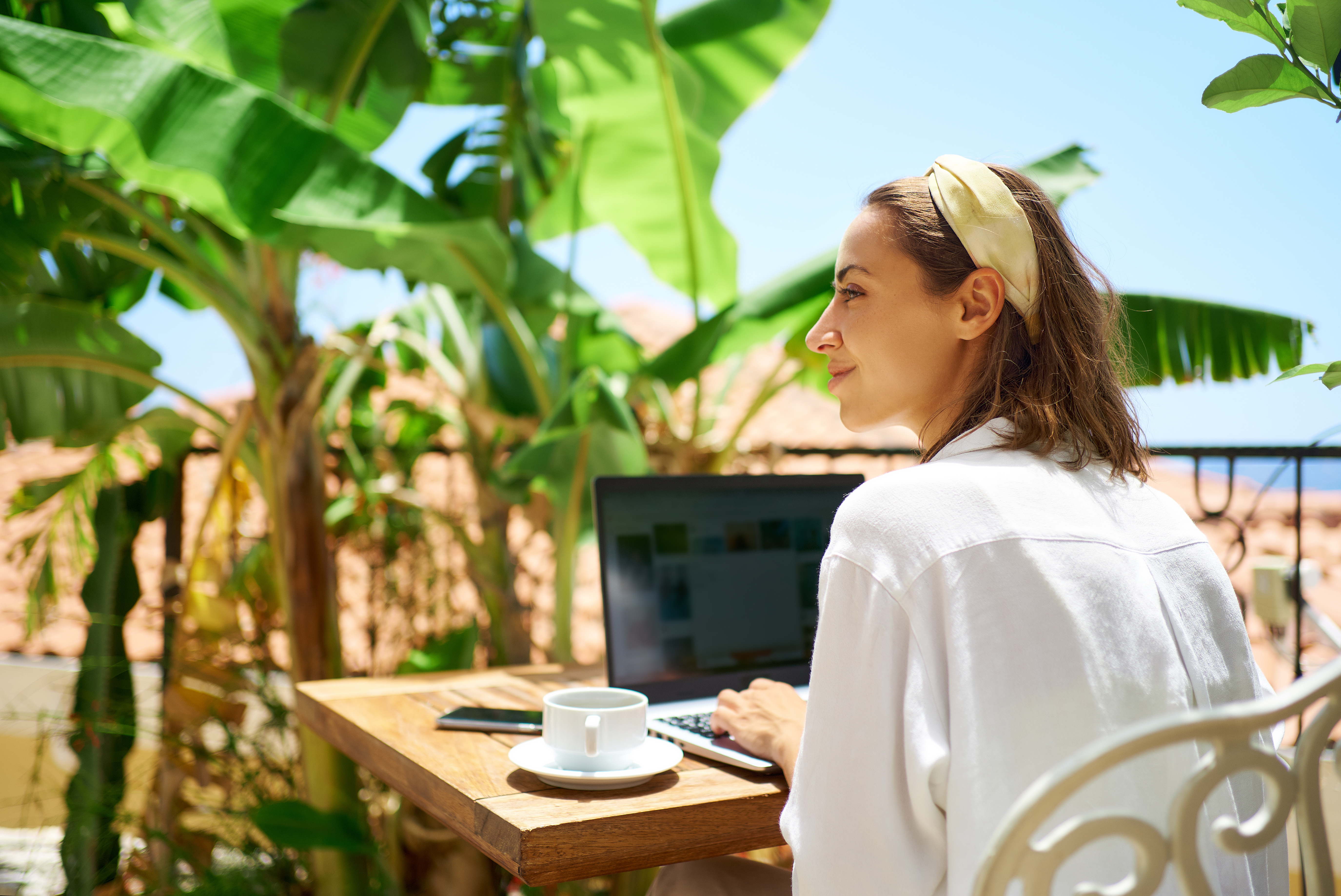 Young woman sitting on terrace at morning during vacation, using laptop computer